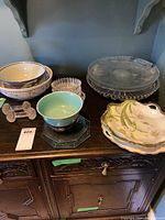 Overview of all items on dark wooden cabinet surface including serving bowls, glass platters, cut glass accessories, and ceramic platters.