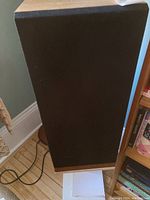 Single Rega Model 3 speaker with black fabric grille on wood-finished stand, showing front view with grille on.