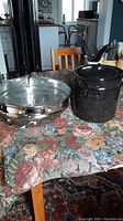 Photo showing the shiny stainless steel multi-tier steamer on the left and a black enamel speckled double boiler on the right with lid.