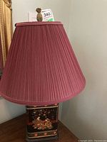 Table lamp with burgundy pleated fabric shade and pineapple-shaped finial on top.