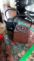 Two cast iron tea pots shown side by side on a floral fabric surface, highlighting their different shapes and finishes.