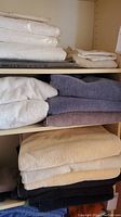 Shelves filled with folded towels of different colors including white, cream, gray, beige, black, and purple.