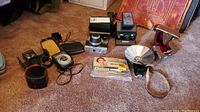 Group shot of two cameras, two light meters, Polaroid flash kit and pack of flashbulbs on carpet