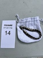 Silver tone men's chain link bracelet displayed on a white drawstring pouch, showing overall length and link style.
