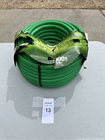 Front view of coiled green garden hose 100 ft with damaged packaging.
