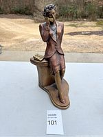 Full side-front view of bronze statue showing woman sitting with phone and book