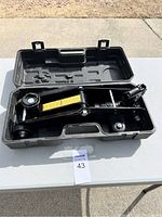 Open plastic carrying case showing the black hydraulic car jack with yellow warning label inside.