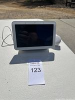 Front view of Google Nest Hub smart display on a table outdoors with screen off and power cable attached.