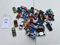 Top-down view of approximately 30 toy cars showing variety of colors and styles, including some recognizable from Disney Cars and typical Hot Wheels looks.