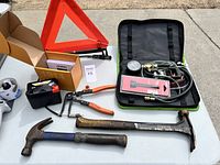Photo of assorted tools including NOCO battery, two hammers, orange handle crimper, red emergency triangle, tire pressure gauge kit in black case.