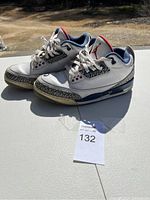 Side and top view of white Nike Air Jordan 3 Retro sneakers with navy and red accents, showing leather upper and elephant print design on the toe and heel.