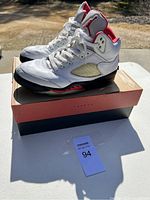 Side profile of the white and red Nike Air Jordan 5 Retro sneakers on top of the shoebox, showing overall condition and design details.