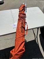 Full view of folded orange beach umbrella with carry bag on an outdoor table