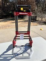 Full front view of the foldable hand truck showing the base plate and telescoping handle in extended position with Milwaukee logo visible.