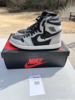 Side profile view of Nike Air Jordan 1 sneakers in black and gray sitting on Nike shoebox outdoors.