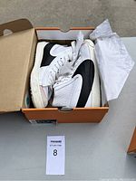 Top view of the pair of white and black Nike sneakers inside an open shoe box with tissue paper, showing signs of wear, size 12.