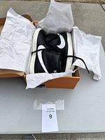 Pair of black and white Nike high top sneakers inside orange shoe box, showing general side angle and shoe paper wrapping.