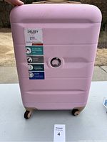 Front view of pink Delsey suitcase showing label with warranty and features.