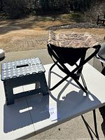 Folding stool with camouflage fabric seat and gray plastic step stool on a white table outdoors.