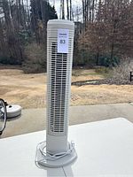 Full height view of the white Holmes tower fan showing the front grille and base with power cord coiled around.