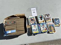 Wide view of baseball card lot in a worn cardboard box with multiple cards spread around it