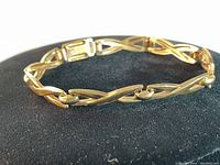 Side angle of gold bracelet showing 'X' pattern links and clasp under natural light.