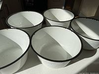 Top-down view of five white enamelled bowls, showing interior and rims with some chipping.