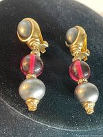 Close-up image of the front of the earrings showing the grey cabochon, pink spherical bead, and grey pearl-like bead with gold-tone metal detailing.