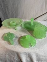 Front view of all five jadeite glass pieces showing candle holder, perfume stopper, sugar bowl lid, handle top, and ribbed piece