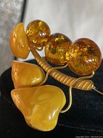 Close-up side angle showing amber and faux butter elements attached to a curved gold-tone stem, showcasing the marbled texture and natural inclusions.