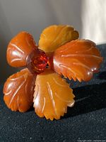 Close-up front and angled views of vintage carved amber brooch with 5 leaves and faceted amber center gemstone.