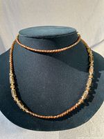 Necklace displayed on a black bust, showing the arrangement of smaller round caramel beads alternating with larger rectangular caramel-hued beads.