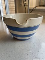 Side angle view of vintage striped ceramic mixing bowl showing blue and cream stripes and pour spout on the rim.