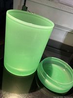 Small vintage jadeite glass jar with matching lid removed, showing interior inside the jar. The jar is translucent green with fine bubbles in the glass surface.