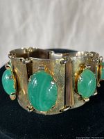 Close-up view of the vintage gold tone bracelet showing green oval cabochon stone set in textured metal link.
