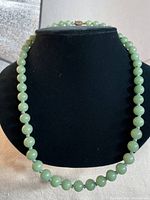 Front view of the entire jade bead necklace displayed on a black bust stand, showing the color and shape of the beads.