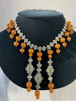 Front view of the vintage ornate silver choker with dangling amber beads displayed on a black bust stand.