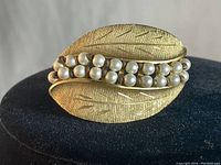 Close-up photo of vintage signed Kramer gold tone brooch with two rows of faux pearls and textured leaf design.