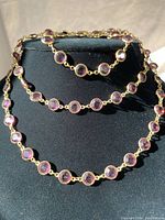 Photo showing the full necklace and bracelet set displayed on a black bust, highlighting the linked round purple crystal stones with gold-tone metal.
