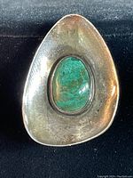 Front angle view of triangular sterling silver brooch featuring a polished green oval stone set in the middle, showing surface patina.