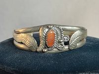 Close-up front view of the vintage sterling Navajo bracelet showing orange stone and leaf stamps.