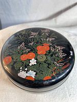 Top view of black lacquer bowl lid showing detailed floral design in red, white, pink, and green.
