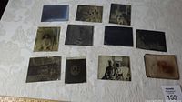 Top view showing all 10 antique glass negative photo plates arranged on a light fabric surface with a measuring tape and sale tag visible.