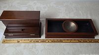 Two wooden boxes placed side by side with measuring ruler beneath showing size; left item is a men's caddy with hinged lids, right is a Bombay wooden jewelry box tray with a metal dish inside.