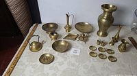 Collection of brass decor items arranged on table including vase, bowls, pitchers, and other pieces.