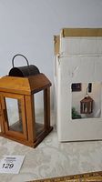 Wooden hanging lantern next to its original box showing the packaging and size reference.