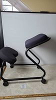 Side view of ergonomic kneeling chair showing cushioned knee rest and seat on a black metal frame with wheels.
