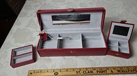 Red genuine leather jewelry box open showing multiple compartments, mirror, and smaller trays and storage sections inside, with a ruler indicating length.