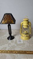 Yellow metal lantern and black metal candle lamp on table, side by side