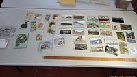View of many postcards spread out on a table with some showing floral artwork, landscapes, urban scenes, and buildings.